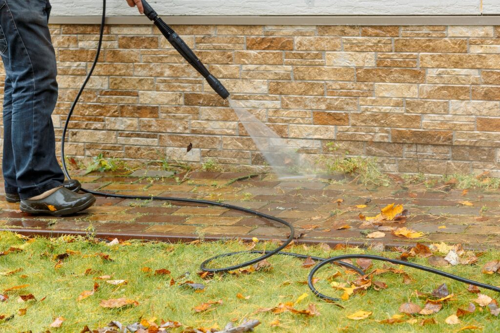 Man cleaning street with high pressure power washer, washing stone garden paths