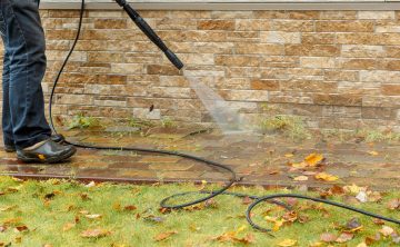 Man cleaning street with high pressure power washer, washing stone garden paths